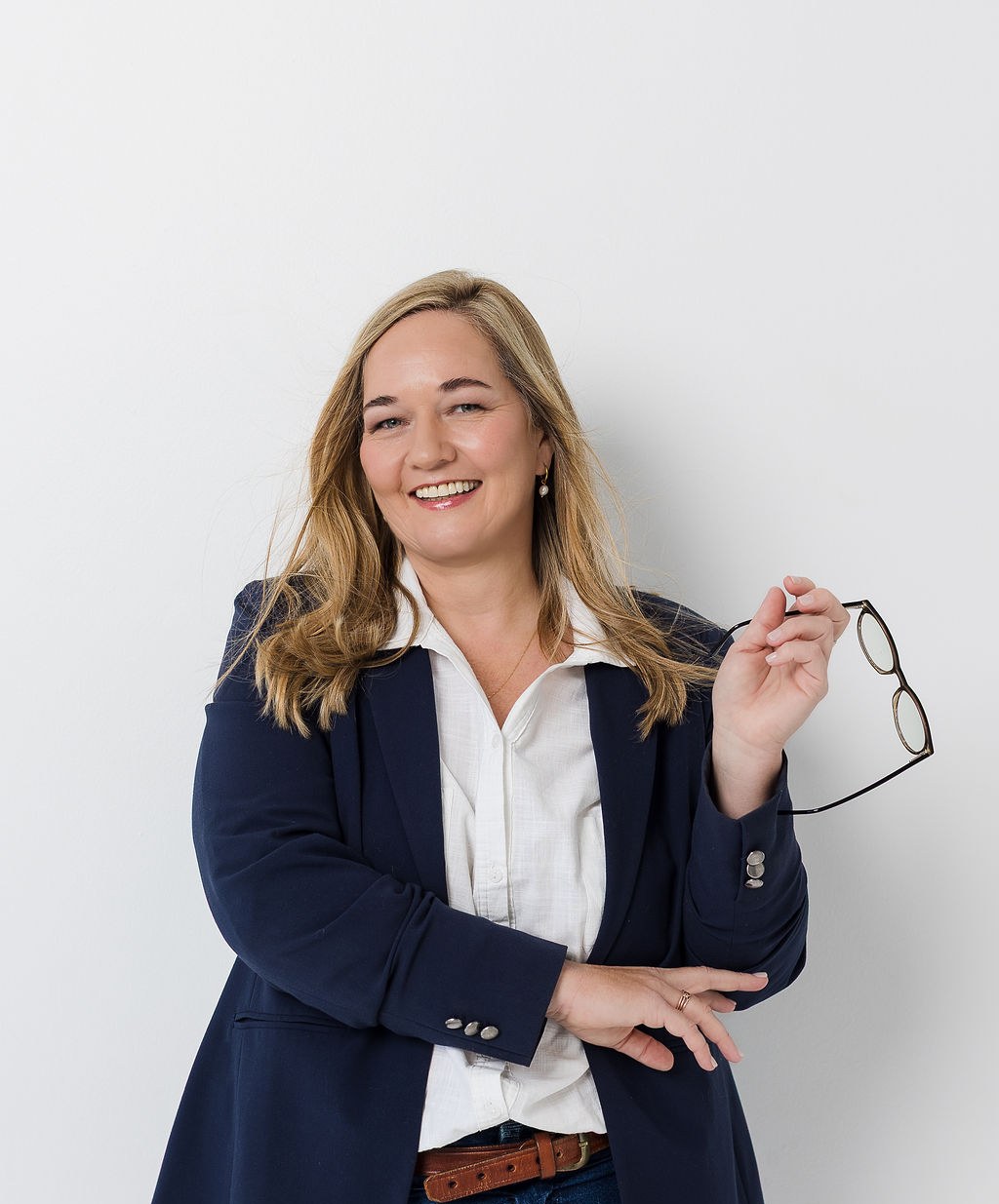 Kobie Abrie, virtual assistant, smiling in a navy blazer holding her glasses